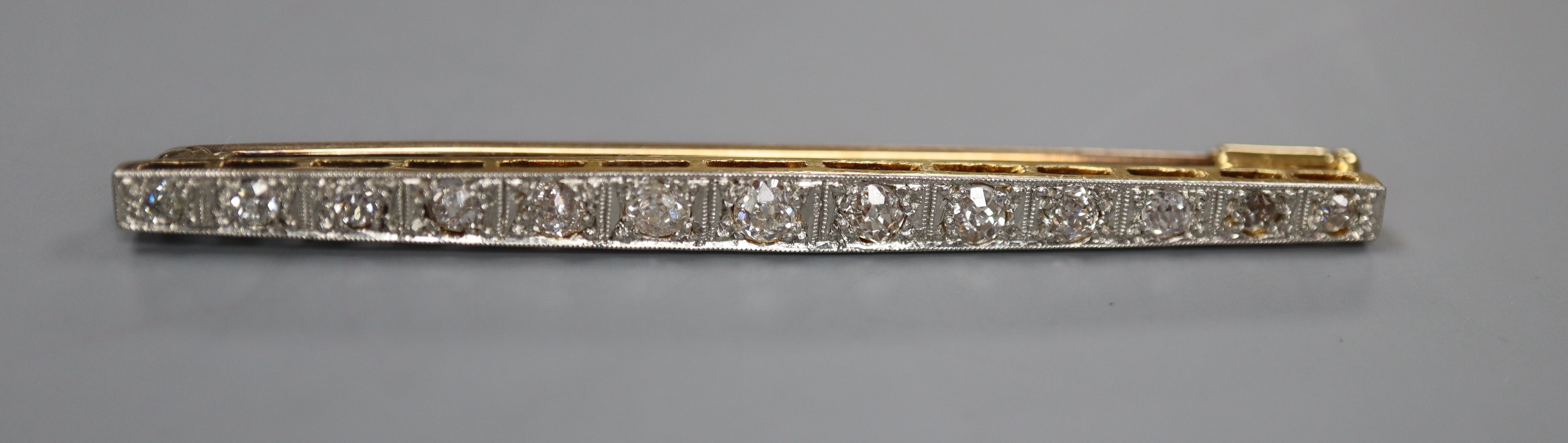 An early 20th century 15ct, plat and graduated thirteen stone diamond set bar brooch, 57mm, gross 4.7 grams.